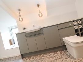 A bathroom with a sink on gray cabinets a toilet and rolls of toilet paper stored in cubbies at Anneth Lowen Angarrack near Hayle