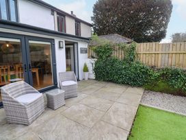 An outdoor patio area with two wicker chairs and a small table next to a white house with sliding glass doors and wooden fence with ivy at Anneth Lowen Angarrack near Hayle