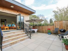 A patio with chairs a table an umbrella and plants outside a wooden house at No1 The Lodge in Acton near Bishops Castle