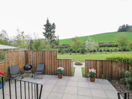A patio with two chairs a barbecue and potted plants overlooking a grassy lawn with trees and hills at No1 The Lodge in Acton near Bishops Castle