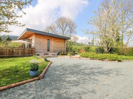 A wooden building with gravel driveway and garden with trees and plants at No1 The Lodge in Acton near Bishops Castle