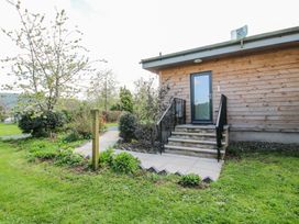 An exterior view of a wooden building with concrete steps leading to a door and a walkway surrounded by grass and bushes at No1 The Lodge in Acton near Bishops Castle