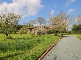 A gravel driveway leading to a wooden cabin surrounded by grassy garden and flowering trees at No1 The Lodge in Acton near Bishops Castle