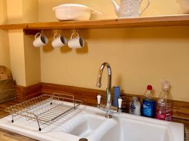 A kitchen with a sink, faucet, dish rack, mugs, and cleaning supplies at Meadow Cottage in Golant, near Fowey