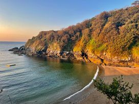 A beach with a cliff and trees at Meadow Cottage in Golant, near Fowey