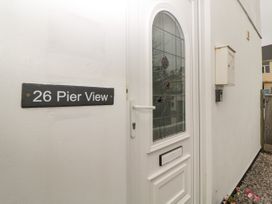A white front door with stained glass and a house number sign on the wall at 26 Pier View in Paighton
