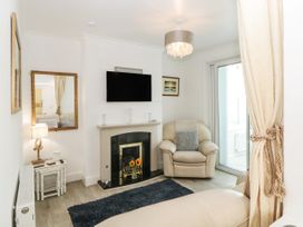 A small living room with a beige armchair a fireplace a wall-mounted TV and a side table with a lamp at Pier View in Paighton