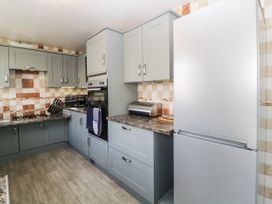 A kitchen with grey cabinets a countertop oven a gas stove a refrigerator and tiled walls at Pier View in Paighton