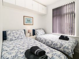 A bedroom with two single beds patterned bedding a nightstand with a lamp under wall cabinets and a window with vertical blinds at Pier View in Paighton