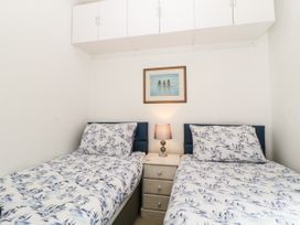 A bedroom with two single beds with patterned bedding a nightstand with a lamp a framed picture above and white overhead cabinets at Pier View in Paighton