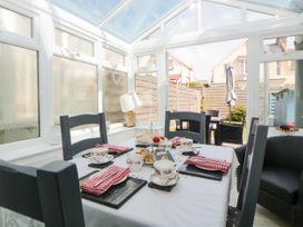 A dining area with a table set for tea and chairs in a conservatory with a view of an outdoor patio at Pier View in Paighton