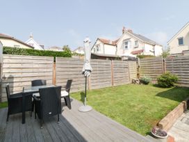 A fenced backyard with a glass table and four black chairs on a wooden deck at Pier View in Paighton