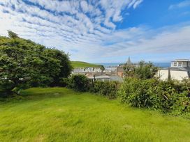 A garden with grass and bushes overlooking buildings and ocean at Crab Cottage Ilfracombe