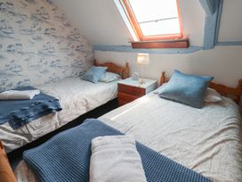 A bedroom with two beds, a bedside table, and a lamp at Delphinium, Blakeney, Norfolk