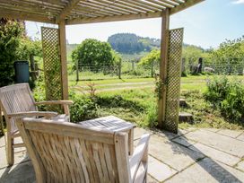 A wooden patio with chairs and table under a pergola overlooking green fields and hills at The Old Beams at Pont y Forwyn Llansantffraidd-ym-Mechain near Welshpool