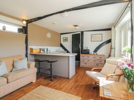 A living room with a kitchen counter, two stools, a sofa, an armchair, a wooden chest of drawers, and flowers on a table at The Old Beams at Pont y Forwyn Llansantffraidd-ym-Mechain near Welshpool