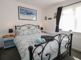 A bedroom with a metal bed frame, floral bedspread, bedside tables with lamps, curtain, and a window at The Old Beams at Pont y Forwyn Llansantffraidd-ym-Mechain near Welshpool