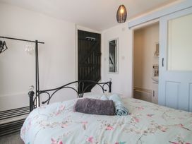 A bedroom with a floral bedspread a black metal bed frame towels on the bed a black clothes rack a black wooden door a mirror on the wall and a sliding door leading to a bathroom at The Old Beams at Pont y Forwyn in Llansantffraidd-ym-Mechain near Welshpool