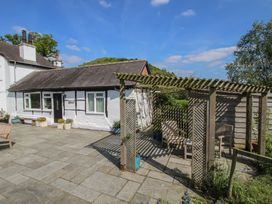 A white cottage with a tiled roof and wooden pergola with chairs on a stone patio at The Old Beams at Pont y Forwyn Llansantffraidd-ym-Mechain near Welshpool