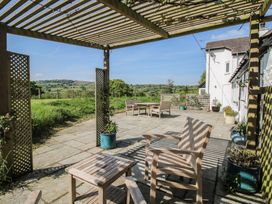 An outdoor patio with wooden chairs and tables under a pergola with plants in pots and a view of fields at The Old Beams at Pont y Forwyn in Llansantffraidd-ym-Mechain near Welshpool