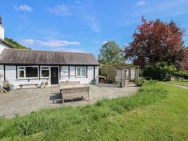 A patio area with wooden benches and a pergola next to a white cottage and a grass lawn at The Old Beams at Pont y Forwyn in Llansantffraidd-ym-Mechain near Welshpool