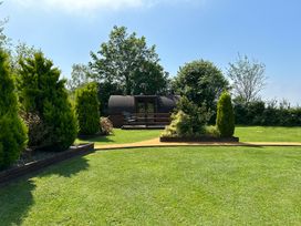 A garden with grass, trees, and a wooden pod at Idris Pod in St Asaph
