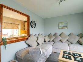A living room with a large sectional sofa and cushions a wall clock and a window opening to a kitchen at Sea Spray in Dinas Dinlle