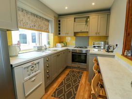 A kitchen with gray cabinets yellow tile backsplash and wooden floor at Sea Spray in Dinas Dinlle