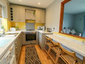 A kitchen with gray cabinets yellow tiled backsplash and wooden chairs at Sea Spray in Dinas Dinlle