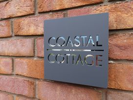 A sign displaying Coastal Cottage on a brick wall