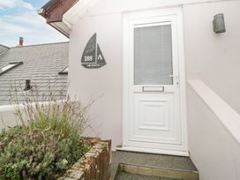 A white door with a sailboat shaped house number plaque next to a brick planter with plants at Monkbarns in Brixham