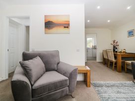 A living room with a gray armchair a wooden side table dining table with chairs and a kitchen visible through a doorway at Monkbarns in Brixham