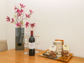 A table with a vase of pink flowers a bottle of red wine two wine glasses and a tray of biscuits and fudge at Monkbarns in Brixham