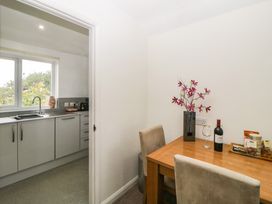 A dining table with two chairs a vase of flowers a bottle of wine and snacks next to a kitchen with cabinets and a window at Monkbarns in Brixham