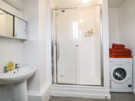 A bathroom with a shower enclosure a sink washing machine and towels stacked on the washing machine at Monkbarns in Brixham