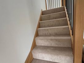 A staircase leading up with carpet steps and wooden handrail at Storws Tanrallt Llanfachraeth