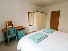 A bedroom with a bed, towels folded on it, desk, chair, and wardrobe at Hafod Wen Pentraeth