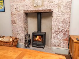A fireplace with a wood stove and a basket of firewood at Gamekeepers Cottage in Chillingham near Chatton