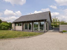 A single story house with large glass windows a gravel driveway and a grass lawn at The Barn at Daubeneys in Colerne