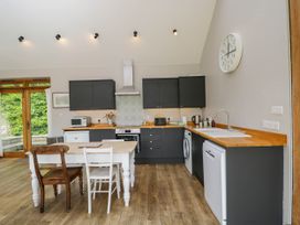 A kitchen with dark cabinets wooden countertops a white table with two chairs a clock on the wall and wooden floor at The Barn at Daubeneys in Colerne