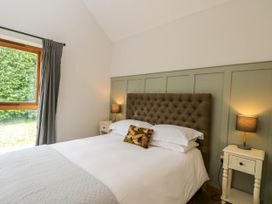 A bedroom with a bed with a tufted headboard two bedside tables with lamps and a window with curtains at The Barn at Daubeneys in Colerne