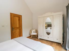 A bedroom with a wooden door a white wardrobe with a mirror and a chair with a cushion at The Barn at Daubeneys in Colerne