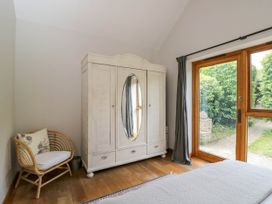 A bedroom with a white wardrobe with mirrored doors a wicker chair wooden floor and glass doors opening to a garden at The Barn at Daubeneys Colerne