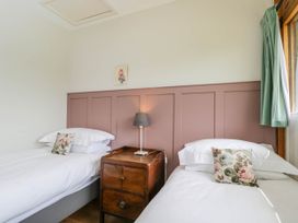 A bedroom with two single beds white bedding and floral pillows a wooden bedside table with a lamp and a window with green curtains at The Barn at Daubeneys in Colerne