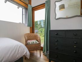 A bedroom with a bed a wicker chair with a cushion a black dresser and a mirror above it at The Barn at Daubeneys Colerne
