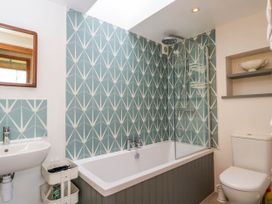 A bathroom with a bathtub shower combination patterned wall tiles toilet and small sink at The Barn at Daubeneys in Colerne