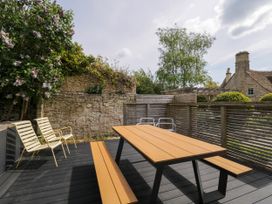 An outdoor patio with wooden picnic table benches and metal chairs surrounded by stone walls and greenery at The Barn at Daubeneys Colerne