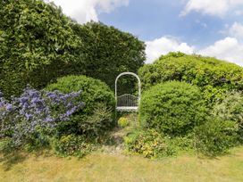 A garden with green bushes blue flowers and a white metal bench at The Barn at Daubeneys Colerne