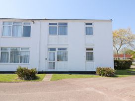A white two-story building with multiple windows and doors surrounded by grass and plants at La Capsule in Dawlish Warren