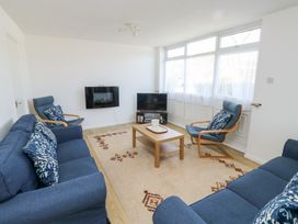 A living room with blue sofas and armchairs around a wooden coffee table near a television at La Capsule in Dawlish Warren